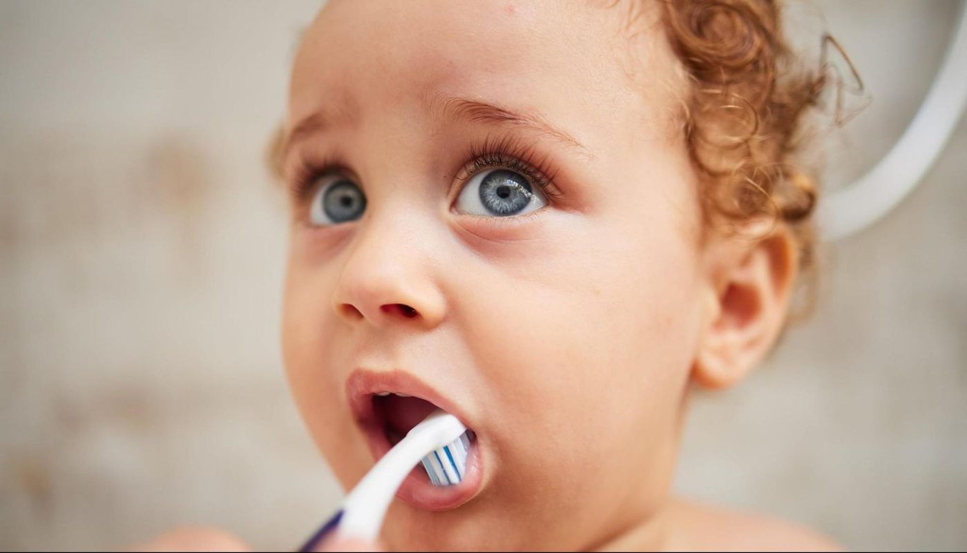 Curly-haired toddler brushing their teeth with a small toothbrush