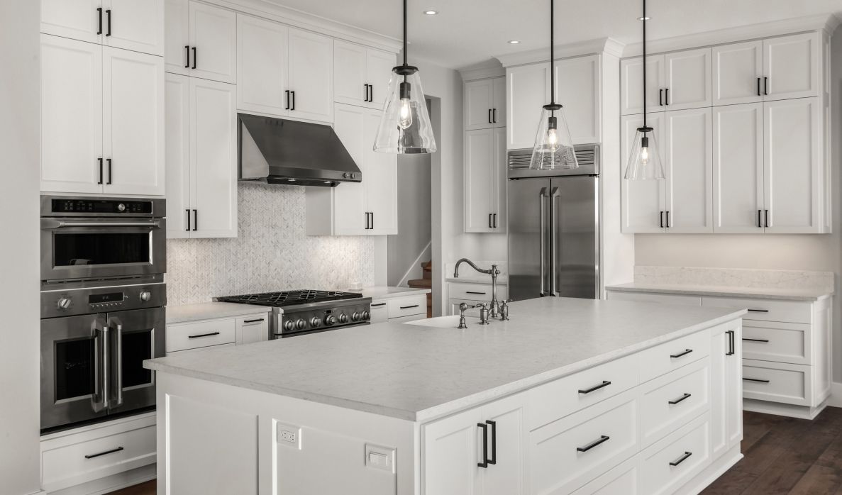 White kitchen with a large island, stainless double wall ovens, and glass pendant lights
