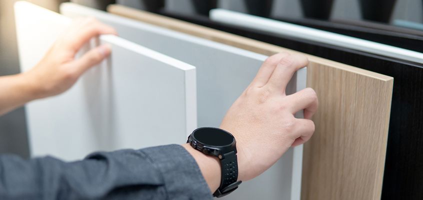 Hands holding cabinet door finish samples in white and wood tones