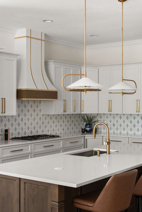 White kitchen with gold pendant lights, a wood-trimmed range hood, and a patterned backsplash