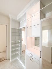 Walk-in closet in Omaha with white TFL finish, LED lighting, glass shelves, drawers with brass hardware, and a full-height mirror. Walk-In Closet with Lighting, Omaha