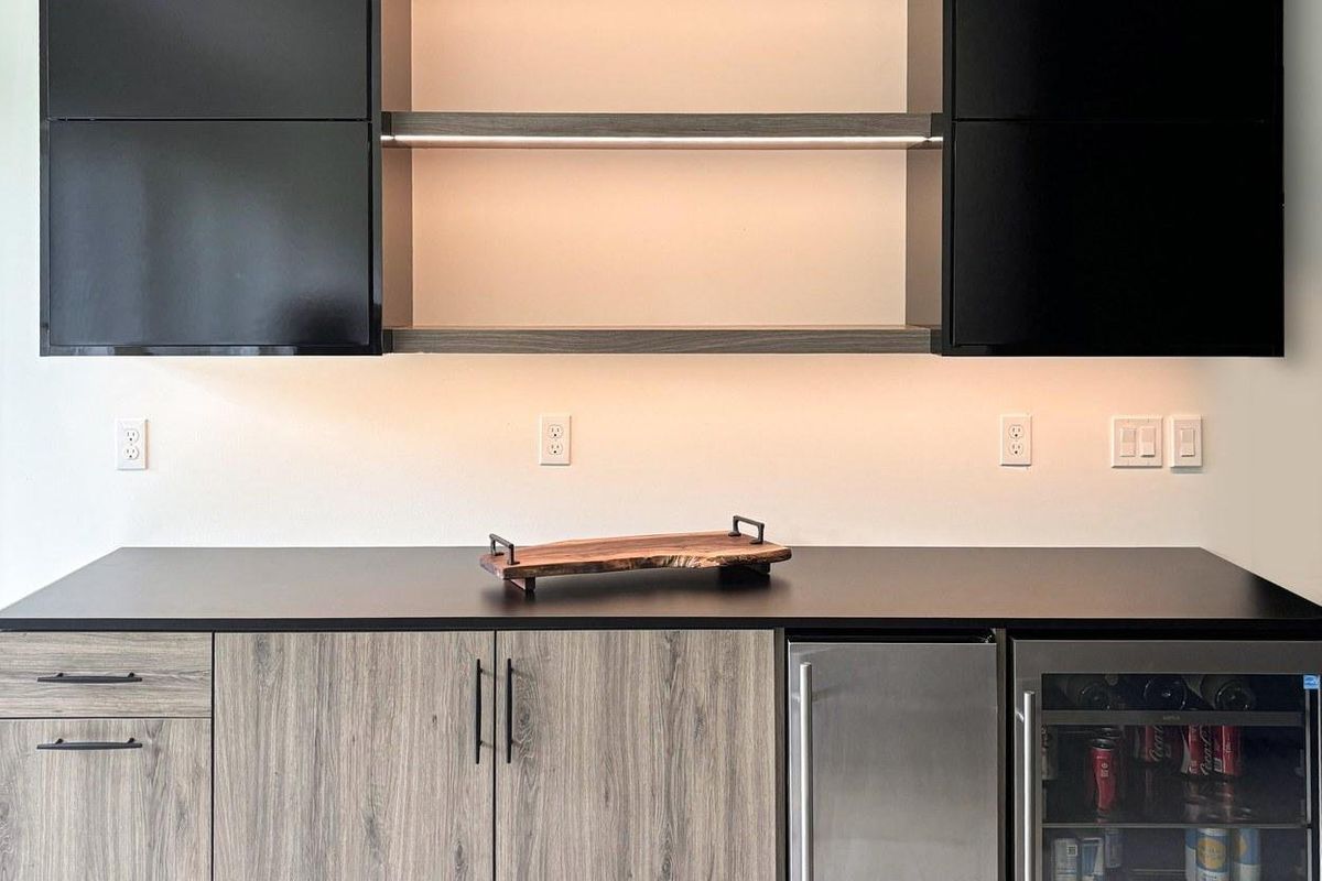 Custom home bar with black upper cabinets, a dark countertop, and a built-in beverage fridge