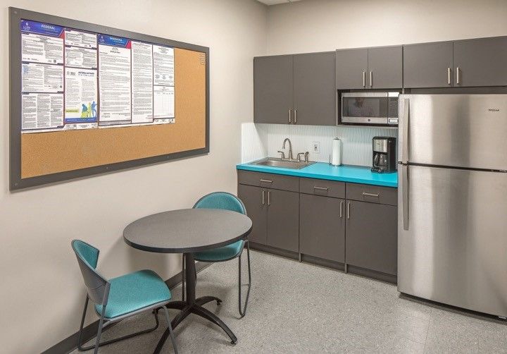 Gray TFL breakroom cabinetry in Omaha with turquoise countertop, upper and lower cabinets, stainless appliances, and adjacent seating area. Commercial Breakroom Cabinetry, Omaha