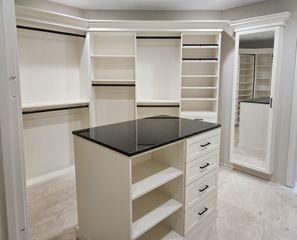 White walk-in closet in Omaha with a center island, full-height hanging sections, a tall mirrored cabinet door, and drawer storage. Custom Walk-In Closet, Omaha