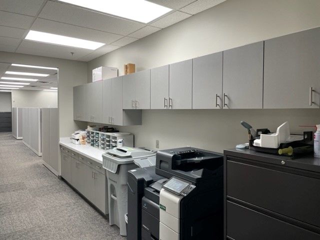 Light TFL commercial cabinetry in Omaha with long upper and lower cabinets, extended countertop, and multiple printers along the workspace wall. Commercial Copy Room Cabinetry, Omaha