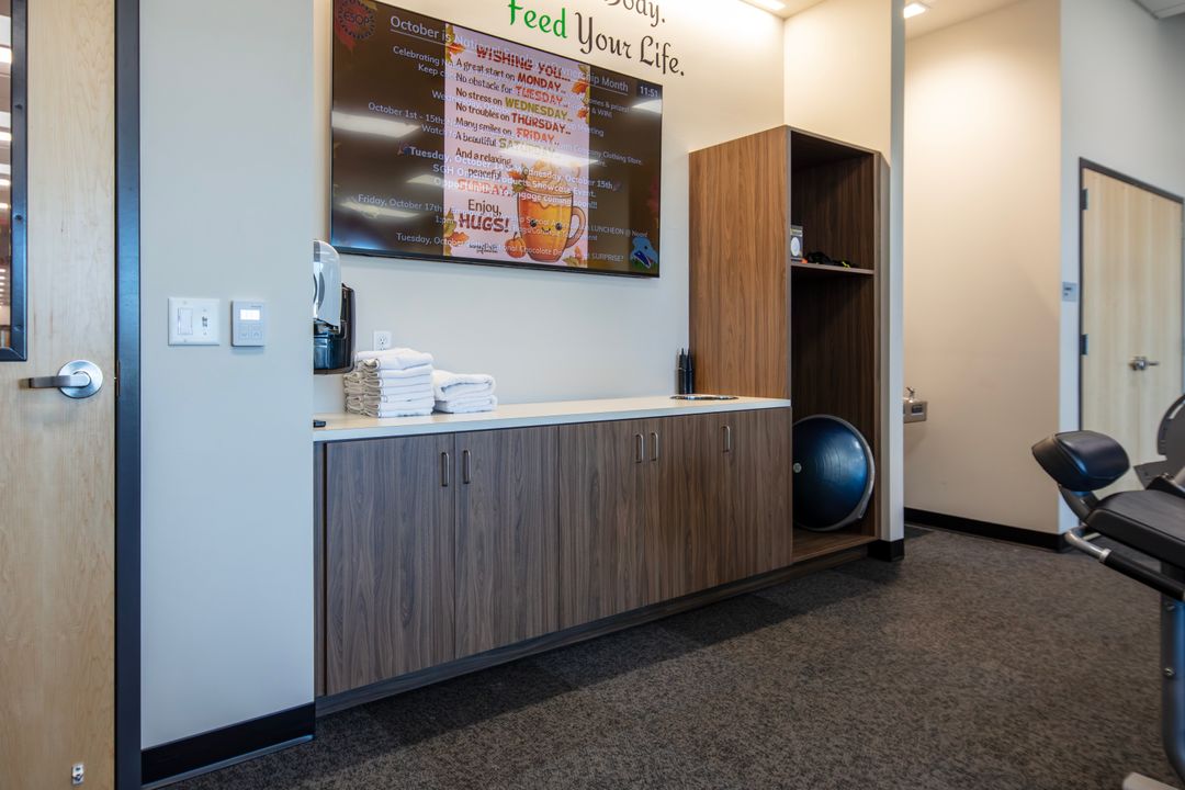 Woodgrain TFL commercial cabinetry in Omaha with lower cabinets, white countertop, and open shelving tower adjacent to fitness equipment. Commercial Storage Cabinetry, Omaha