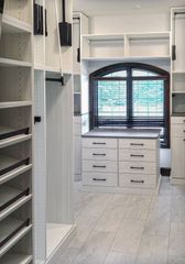 Walk-in closet in Omaha with white woodgrain cabinetry, center island drawers, open shelving, and hanging storage around a window. Custom Walk-In Closet with Island, Omaha