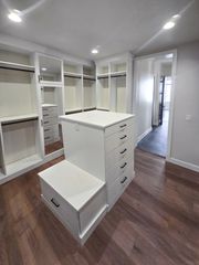 This spacious walk-in closet by Incontro Closets showcases a sleek, modern design with a central island featuring drawers and an integrated seating nook. Ample hanging space, open shelving, and a full-length built-in mirror make this the ultimate in luxury closet organization. Modern Walk-In Closet with Center Island and Built-In Mirror | Incontro Closets