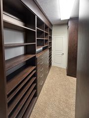 Walk-in closet in Omaha with dark woodgrain finish, open shelving, stacked drawers, and wide shoe shelves. Walk-In Closet with Dark Wood Shelving, Omaha