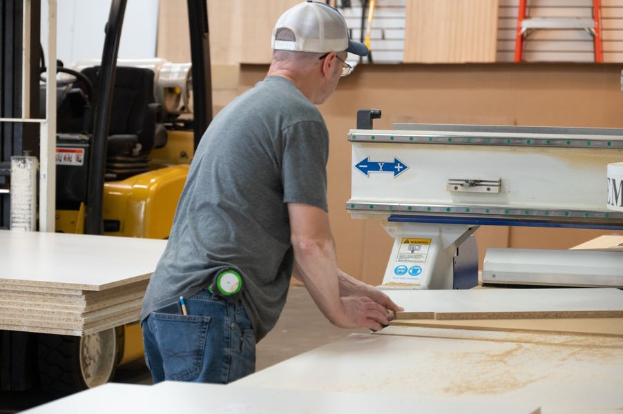 Incontro Closets team member working at a panel saw in the Omaha shop, trimming material with woodworking equipment and stacked boards nearby. Shop Fabrication, Omaha