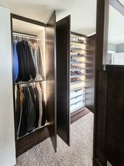 Walk-in closet in Omaha with dark woodgrain TFL wardrobes, interior hanging sections with LED lighting, and an adjacent shoe wall. Walk-In Closet Storage, Omaha