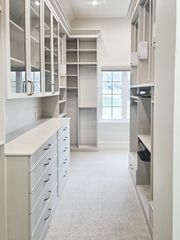 Light-toned walk-in closet in Omaha with glass-front shaker-style cabinets, a long drawer base, and open shelving along both sides. Custom Walk-In Closet, Omaha