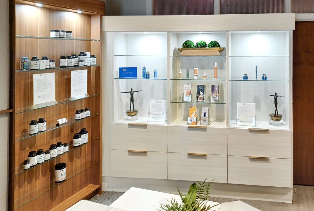 Alt description: White TFL commercial display cabinetry in Omaha with glass shelves, integrated lighting, lower drawers, and adjacent woodgrain wall shelving for retail products. Commercial Display Cabinetry, Omaha