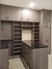 Walk-in closet in Omaha with woodgrain TFL finish, black stone countertop island, shoe shelving, and upper storage cabinets. Walk-In Closet with Island and Cabinets, Omaha