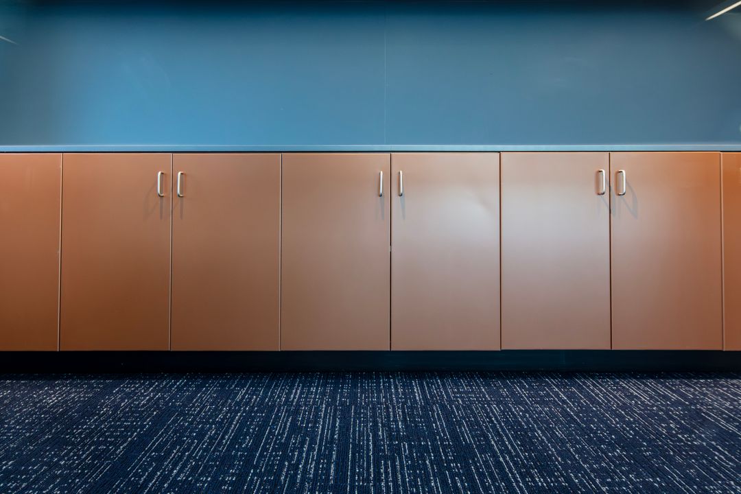 Warm-toned TFL commercial cabinets in Omaha with silver pulls installed in a long run beneath a blue accent wall. Commercial Cabinets, Omaha