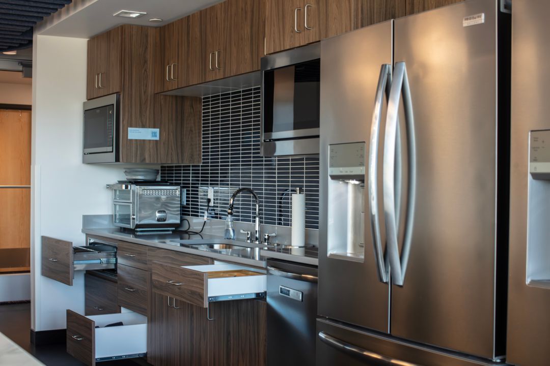 Woodgrain TFL commercial kitchenette in Omaha with open drawers, stainless appliances, black tile backsplash, and upper and lower cabinets. Commercial Kitchenette, Omaha