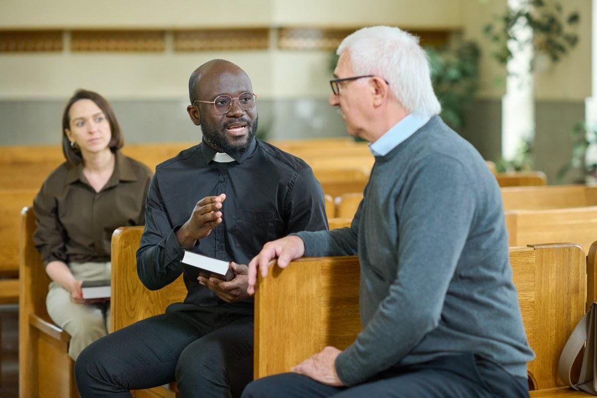 Priest talking with parishioners in the pews about planned giving for churches