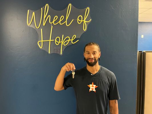 Former pro baseball player holding keys to his new home under a Wheel of Hope sign