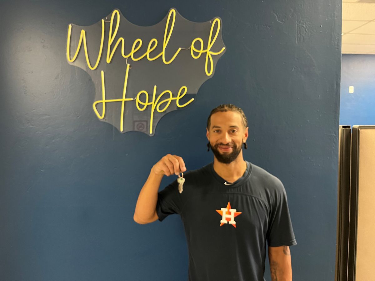 Former pro baseball player holding keys to his new home under a Wheel of Hope sign