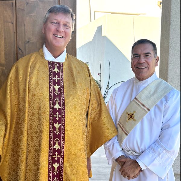 Priest and deacon in vestments smiling outside a church