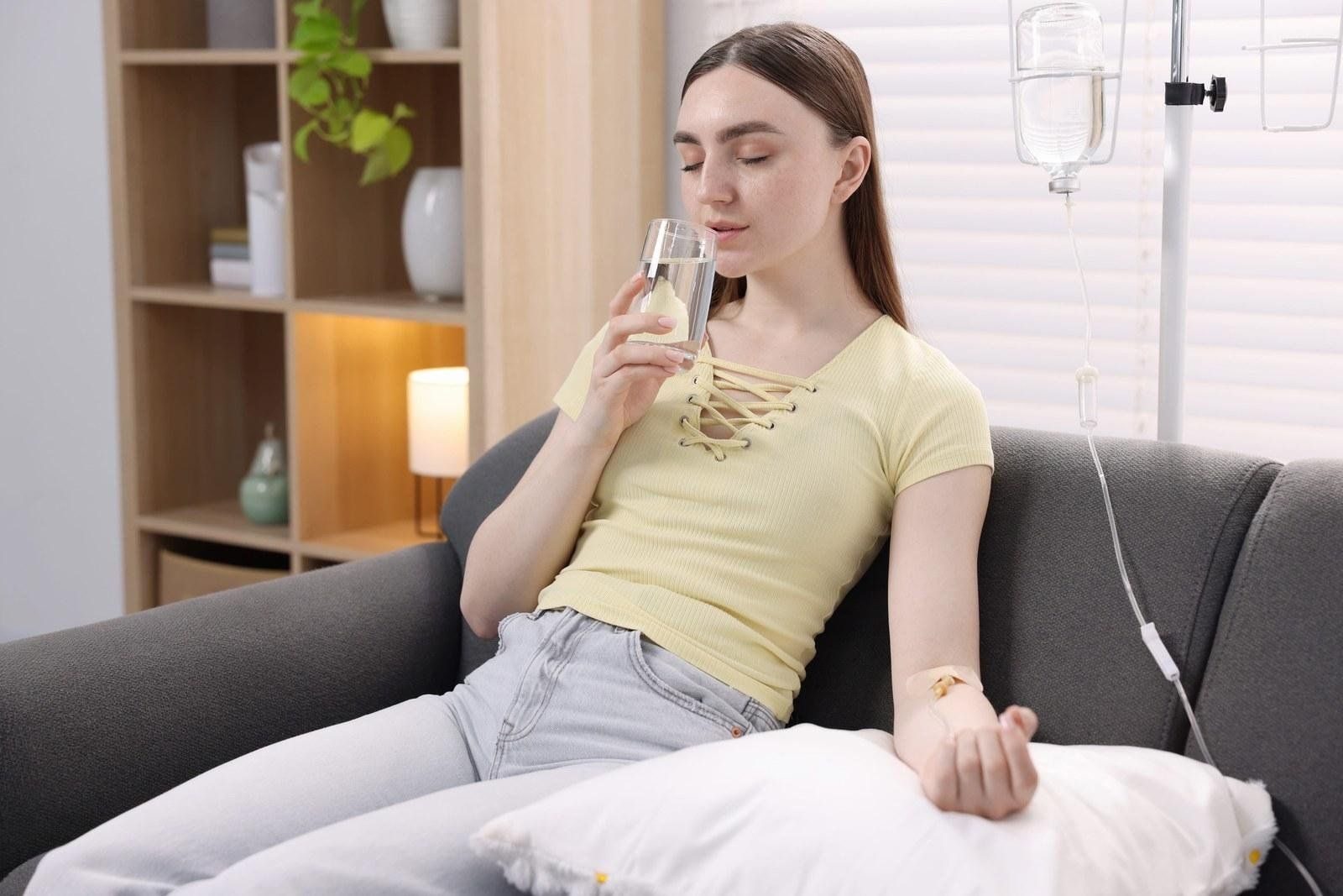 Woman relaxing on a sofa and sipping water while receiving an immune boost IV drip