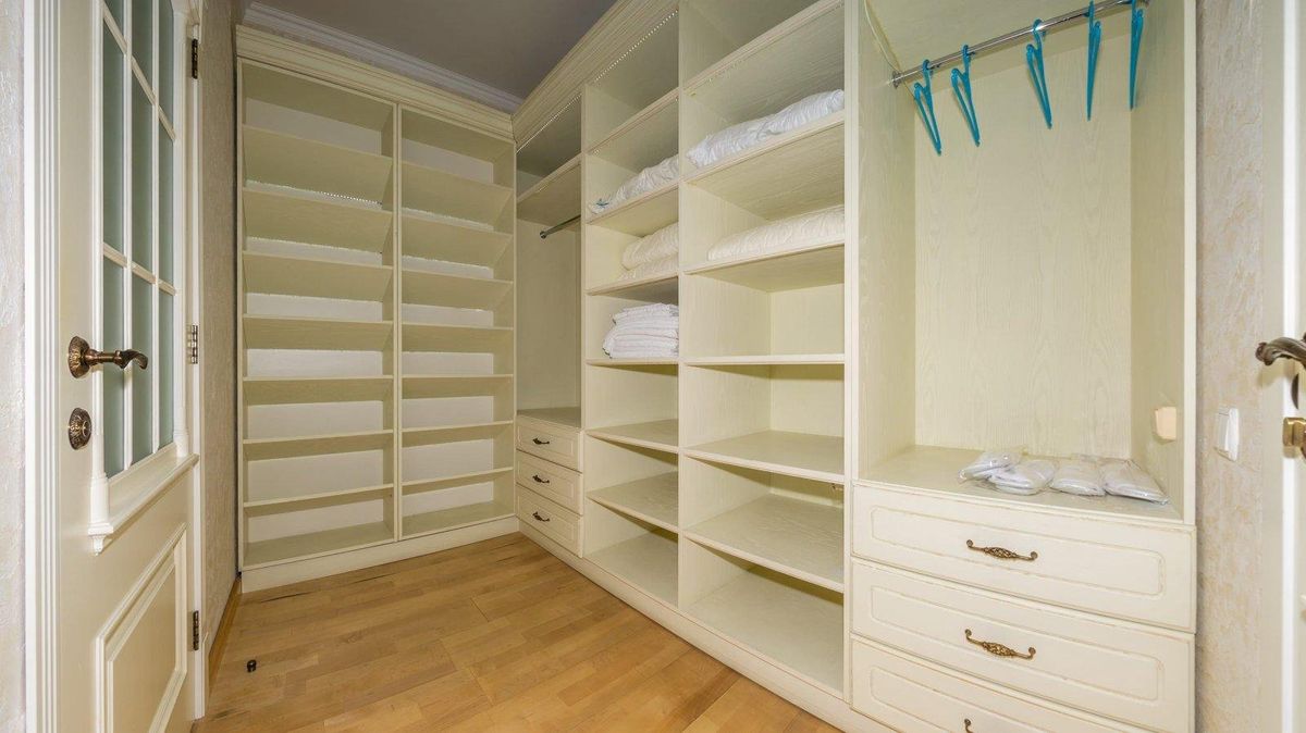 Empty walk-in closet with cream built-in shelves, drawers, and hanging rods