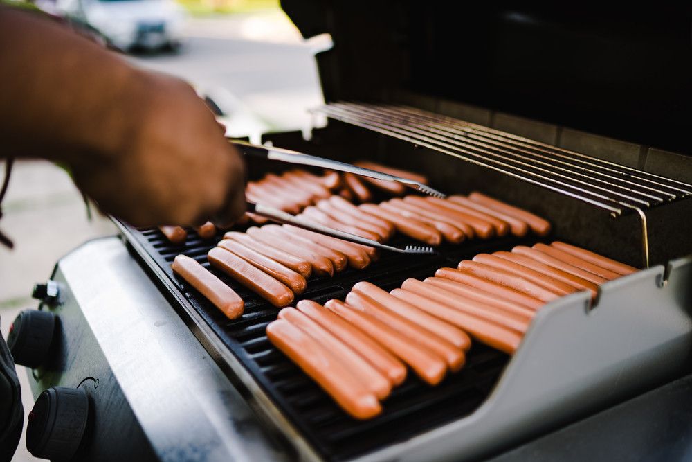 Man turning hot dogs on a gas grill