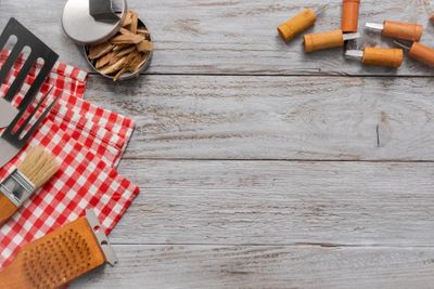 Grilling tools, wood chips, and a red checked towel laid out on a weathered wood table